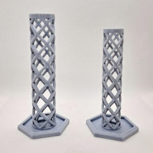 May include: Two gray, lattice-patterned candle holders. Each holder has a hexagonal base and a cylindrical body with a repeating diamond design. The candle holders are made of a 3D-printed material.