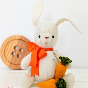 May include: A white felt bunny rabbit toy with orange ribbon and two orange felt carrots. The bunny has embroidered eyes and a nose.