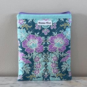 May include: A quilted fabric case with a floral pattern in teal, purple, and light blue. The case has a teal zipper and trim. The label "Bobbin Fred" is visible on the front. The case is designed to hold a tablet or e-reader.