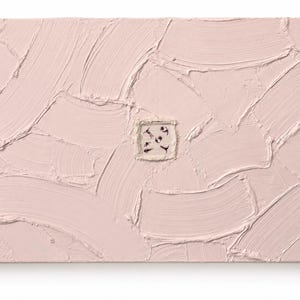May include: A rectangular abstract painting with a textured, light pink surface. The surface has visible brushstrokes. A small, square, off-white patch with black markings is centered on the painting.