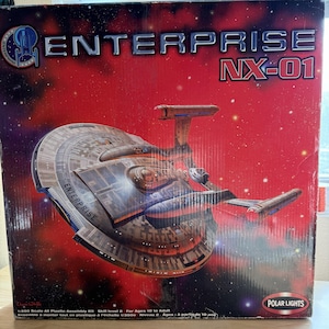 May include: A model kit box for the Enterprise NX-01 starship. The box is red with the ship prominently displayed. The ship is gray and brown with the word "ENTERPRISE" printed on the side. The box also includes the text "NX-01" and "POLAR LIGHTS".