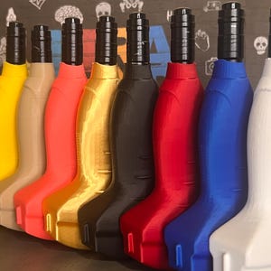 May include: A row of eight colorful bottle stoppers. The stoppers are in shades of yellow, tan, coral, gold, black, red, blue, and white. Each stopper has a black top and a curved, ergonomic design.