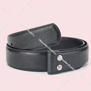 May include: A black leather belt with a textured surface. The belt has a buckle-less design with two silver-colored button details. The belt is curved and appears to be new.