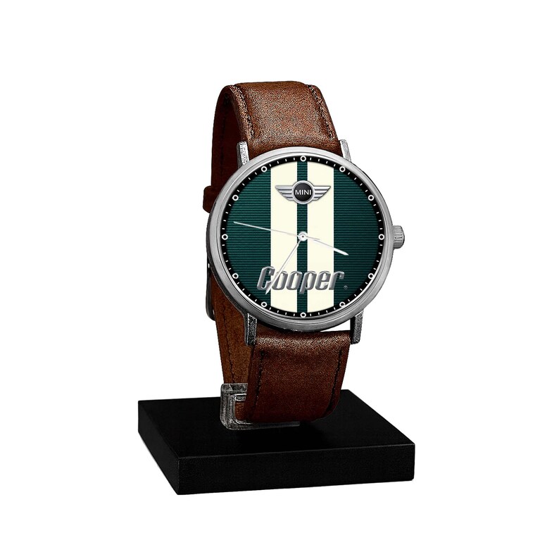 May include: A wristwatch with a brown leather band and a silver-colored case. The watch face is green with two white stripes and the word "Cooper" in white. The watch is displayed on a black stand.
