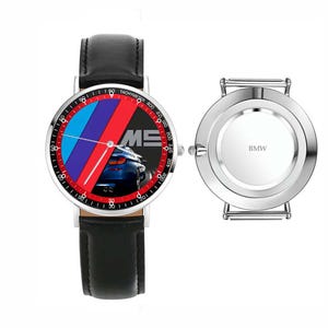 May include: A wristwatch with a black leather band and a silver-colored case. The watch face features the BMW logo in blue, red, and black, with a car image and the letters "M5". The back of the watch is silver with the word "BMW".