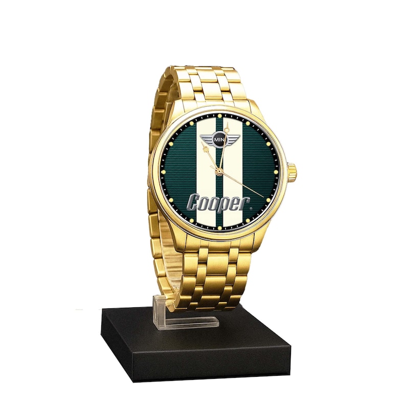 May include: A gold-toned wristwatch with a green and white face, featuring the "MINI Cooper" logo. The watch has a gold band and is displayed on a black stand. The watch face has a green background with two white vertical stripes and the word "Cooper".