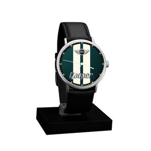 May include: A black leather-banded watch with a silver case. The watch face is dark green with two white vertical stripes and the word "Cooper" in white. The watch has the Mini logo and is displayed on a black stand.