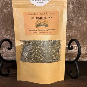 May include: A brown paper bag with a clear window, filled with dried herbs. The bag has a label that reads "FLU FIGHTER TEA" and "Immune & Respiratory Support." A white sticker at the top says "Quality & Safety Seal. Do Not Use if Seal is Broken."