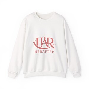Peut inclure: Un sweat-shirt blanc à col rond avec le mot "HAR" en rose-rouge stylisé, et le mot "HERAFTER" en dessous. Le design comprend des accents en forme d'étoiles. Le sweat-shirt est en matière douce.