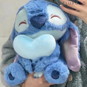 May include: A plush blue stuffed animal with large ears, a light blue nose, and dark blue spots. The toy has a soft, furry texture and closed eyes. The word "ELUROSO" is visible in the top right corner.