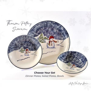 May include: Thomson Pottery Snowman dinnerware set including dinner plates, salad plates, and bowls. Each piece features a cream-colored base with a dark blue speckled sky, green pine trees, and a snowman wearing a red hat and scarf. Text reads: Thomson Pottery Snowman, Choose Your Set, Dinner Plates, Salad Plates, Bowls, and Artful Vintage Home.