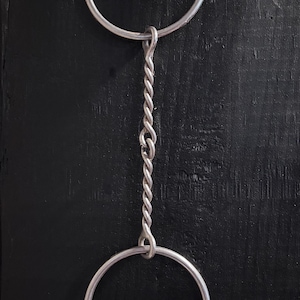 May include: A silver metal chain with two circular rings connected by a twisted chain. The top ring is attached to a screw. The background is a dark, textured surface.