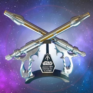 Puede incluir: Un par de blasters Westar 34 plateados y dorados de Star Wars, cruzados y montados sobre un soporte negro. El soporte presenta un logotipo de Star Wars y el texto "Jango Fett". El fondo es una galaxia púrpura y azul.