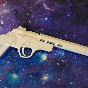 May include: A white plastic toy blaster with a long barrel, a textured grip, and a trigger guard. The object features a futuristic design with geometric paneling and vents along the top of the barrel, presented in a solid, matte white finish.