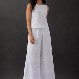 May include: A white two-piece set consisting of a sleeveless top and wide-leg trousers. Both pieces are crafted from fabric featuring an intricate tonal eyelet embroidery pattern with scalloped edges along the hemline and waistline.