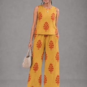 May include: A mustard yellow sleeveless top and matching wide-leg trousers set featuring a repeating burnt orange floral block print pattern. The top has a round neckline and the trousers have a relaxed fit with a consistent botanical motif throughout.