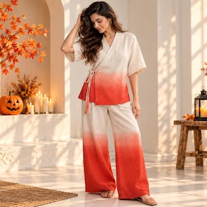 May include: A two-piece lounge set consisting of a wrap-style top with half-length sleeves and wide-leg trousers. The garment features an off-white base colour that transitions into a vibrant orange-red ombre gradient at the hem of both pieces.