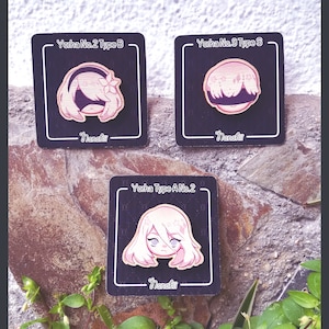 May include: Three wooden pins featuring anime characters with pink and white hair. The pins are on a background of brown rock and green plants. The text on the pins reads "Yorha No.2 Type B", "Yorha No.9 Type S", and "Yorha Type A No.2".
