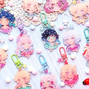Puede incluir: Una colección de 12 abalorios de personajes coloridos con llaveros. Los abalorios presentan personajes de estilo anime con diferentes colores de cabello, atuendos y expresiones. Los abalorios están hechos de acrílico transparente y tienen un acabado brillante.
