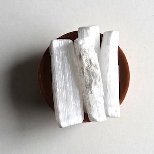 May include: Four white selenite sticks in a small brown bowl. The sticks are smooth and have a striated texture.