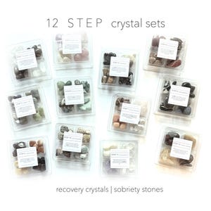 Puede incluir: Doce recipientes de plástico transparente, cada uno dividido en cuatro secciones, llenos de varios cristales coloridos. Cada contenedor tiene una etiqueta blanca con texto. El texto "12 STEP crystal sets" y "recovery crystals | sobriety stones" también son visibles.