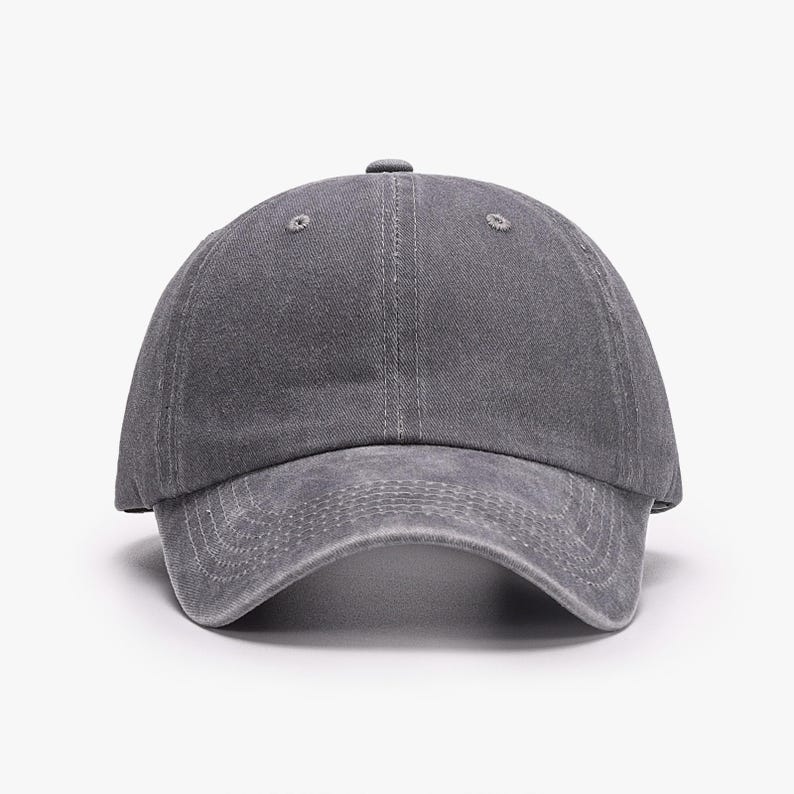 May include: A solid charcoal gray baseball cap with a distressed, washed-out fabric texture. The cap features a six-panel construction with a curved brim, stitched eyelets on the crown, and visible tonal stitching along the front visor panels.