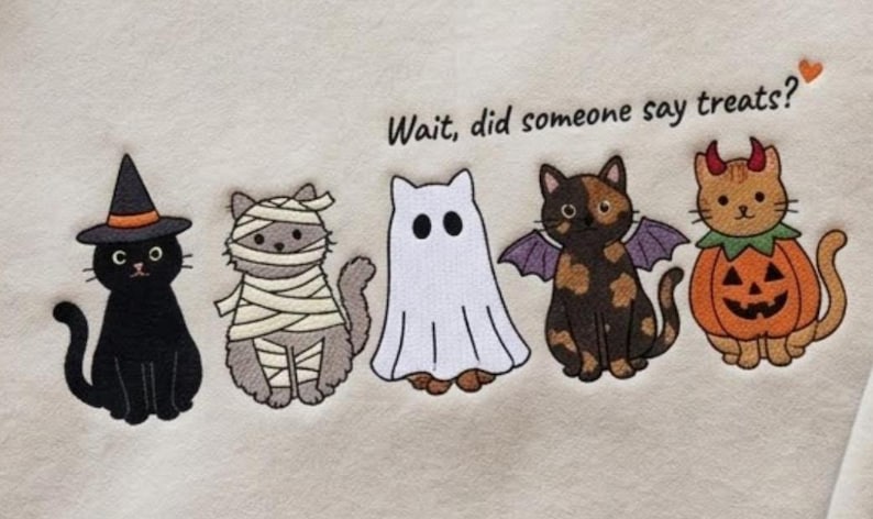 May include: A cream-colored fabric featuring an embroidered graphic of five cats in Halloween costumes: a black cat in a witch hat, a gray mummy cat, a white ghost cat, a tortoiseshell bat cat, and an orange pumpkin cat with the text Wait, did someone say treats?