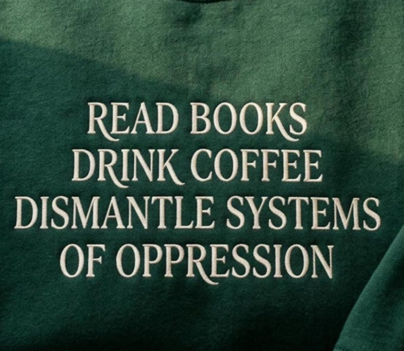Op de afbeelding: Een donker bosgroen sweatshirt met witte geborduurde tekst die luidt: READ BOOKS DRINK COFFEE DISMANTLE SYSTEMS OF OPPRESSION. De stof heeft een zachte, fleece-achtige textuur en de tekst is gecentreerd in een strak, schreefloos lettertype.