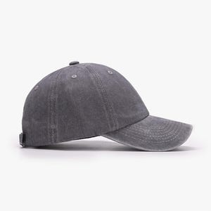 May include: A charcoal gray baseball cap with a washed, distressed fabric finish. The cap features a six-panel construction with stitched eyelets, a curved brim with horizontal stitching, and a small fabric-covered button at the crown center.
