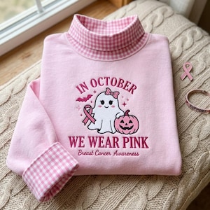 Op de afbeelding: Een lichtroze sweatshirt met een opstaande kraag in een roze en wit vichy-ruitpatroon. De mouwboorden hebben ook een bijpassend vichy-patroon. Op de voorkant is een geest met een roze strik, een roze pompoen en een roze lint geborduurd.
