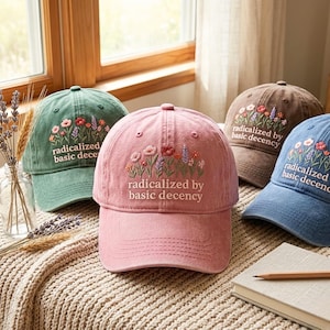 Puede incluir: Cuatro gorras de béisbol en verde salvia, rosa empolvado, marrón y azul pizarra. Cada gorra presenta flores silvestres bordadas y el texto "radicalized by basic decency" en hilo blanco. Tienen una visera curva y un diseño de seis paneles.