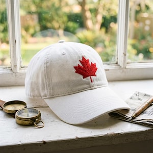 Peut inclure: Une casquette de baseball blanche avec une feuille d'érable rouge brodée sur le panneau avant. La casquette présente une visière incurvée et une calotte structurée avec des œillets cousus. Le motif est centré sur l'avant de la casquette.