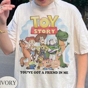 Puede incluir: Camiseta de color marfil con un gr&aacute;fico colorido de personajes de la pel&iacute;cula animada "Toy Story". El dise&ntilde;o incluye el t&iacute;tulo de la pel&iacute;cula y la frase "You've Got a Friend in Me".