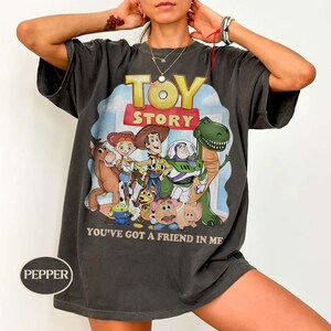 Puede incluir: Camiseta gris oscuro con el logotipo y los personajes de Toy Story. El gr&aacute;fico incluye a Woody, Buzz Lightyear y otros personajes de la pel&iacute;cula animada. Tambi&eacute;n se muestra el texto "YOU'VE GOT A FRIEND IN ME".