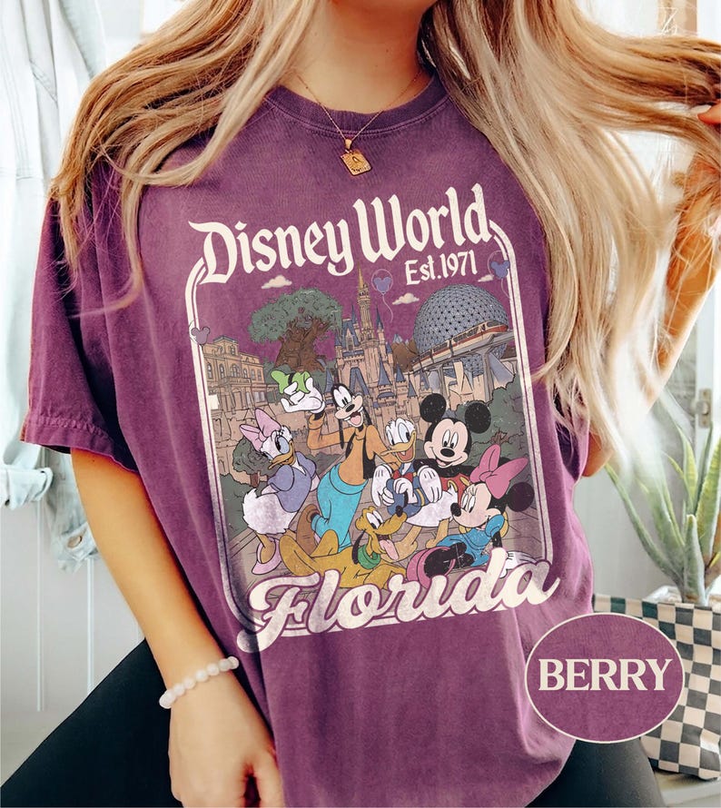 May include: Berry-colored t-shirt featuring a Disney World graphic. The graphic includes the text "Disney World Est. 1971" and a colorful illustration of Disney characters and landmarks. The word "Florida" is also displayed.