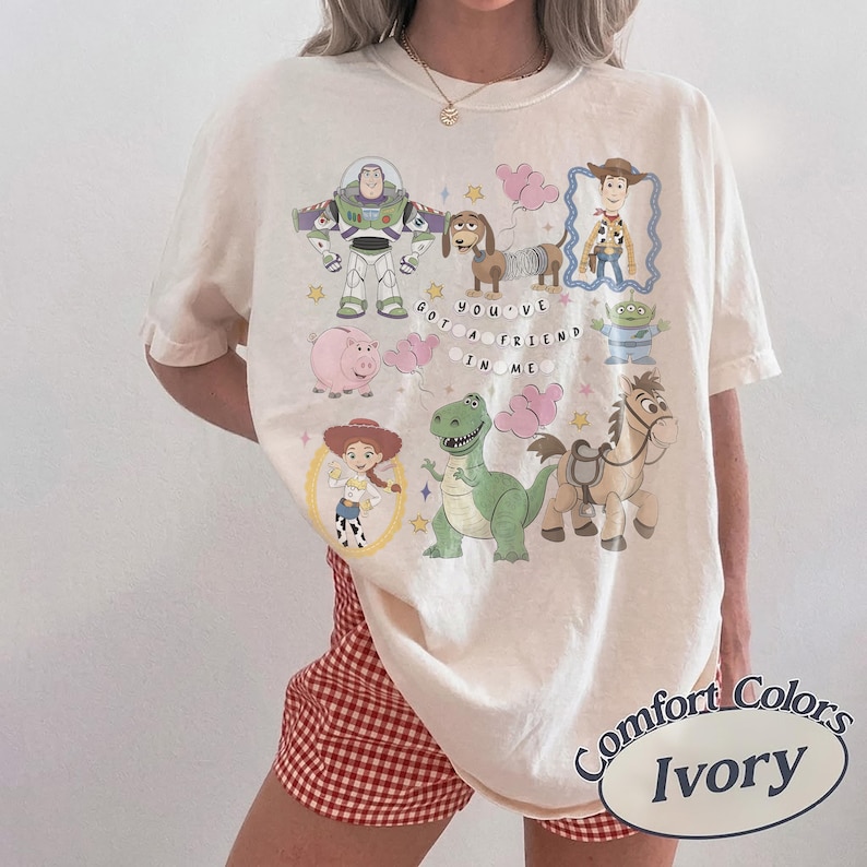 Pu&ograve; includere: T-shirt color avorio con personaggi dei cartoni animati di un popolare film d'animazione. Il design include Buzz Lightyear, Woody, Jessie, Rex, Hamm, Slinky Dog, Bullseye e i piccoli omini verdi. Viene visualizzata anche la frase "YOU'VE GOT A FRIEND IN ME".