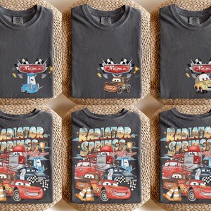 May include: Six dark grey t-shirts with various designs. The top row features cartoon cars with the word "Name" above them. The bottom row has a design with the words "Radiator Springs" and various cartoon cars.