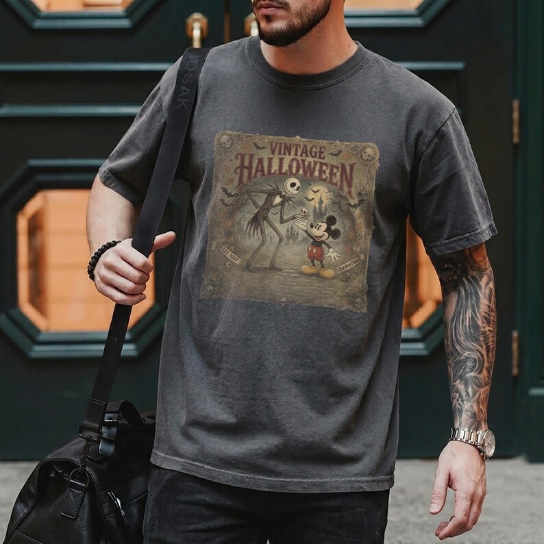 May include: A charcoal gray short-sleeve t-shirt featuring a graphic print with the text "VINTAGE HALLOWEEN". The design depicts Jack Skellington and Mickey Mouse standing in front of a castle, surrounded by bats and skulls in a muted color palette.