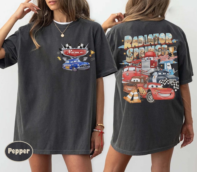 May include: Dark grey t-shirt with a front graphic of a blue car and the word "Name". The back of the shirt has a colourful graphic of cartoon cars and the text "Radiator Springs".