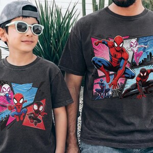 K&ouml;nnte beinhalten: Zwei anthrazitfarbene T-Shirts mit einer Comic-Grafik von Spider-Man und anderen Spider-Verse-Charakteren. Die Shirts werden von einem Kind und einem Erwachsenen getragen, was auf ein passendes Set hindeutet.