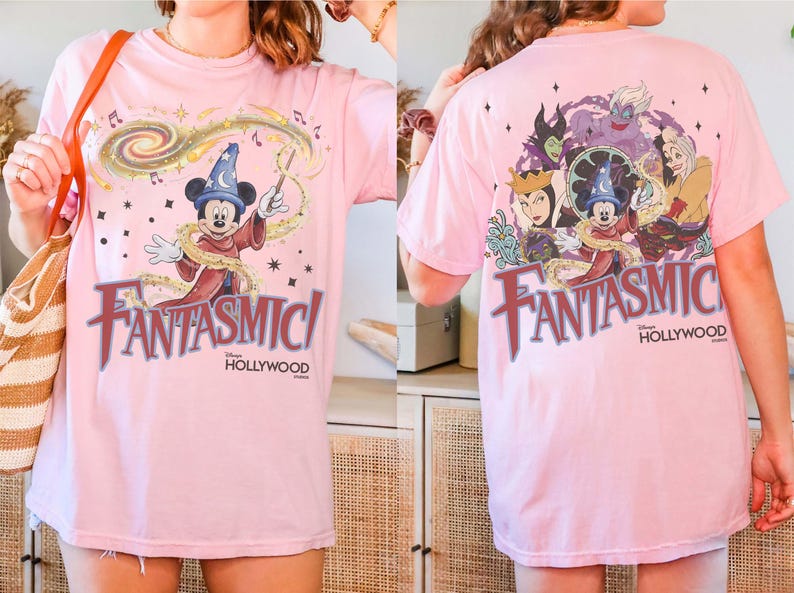 May include: Pink t-shirt featuring Mickey Mouse as a sorcerer with the text "Fantasmic!" in a stylized font. The back of the shirt displays various Disney villains. The shirt is a light pink color.