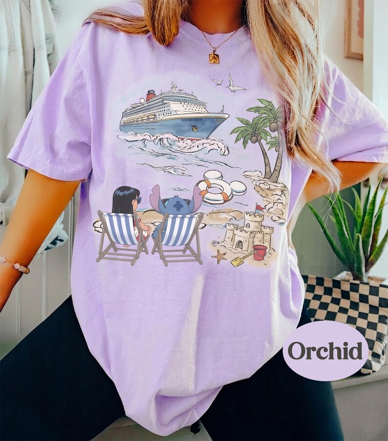 May include: A light purple t-shirt featuring a cruise ship on the ocean, palm trees, and a beach scene with cartoon characters. The shirt has a relaxed fit and the word "Orchid" printed on the bottom right.