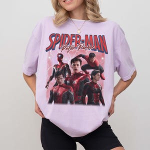 May include: A lilac t-shirt with a graphic of Spider-Man and the text "SPIDER-MAN Peter Parker" in red and blue. The graphic shows multiple images of Spider-Man in action poses.