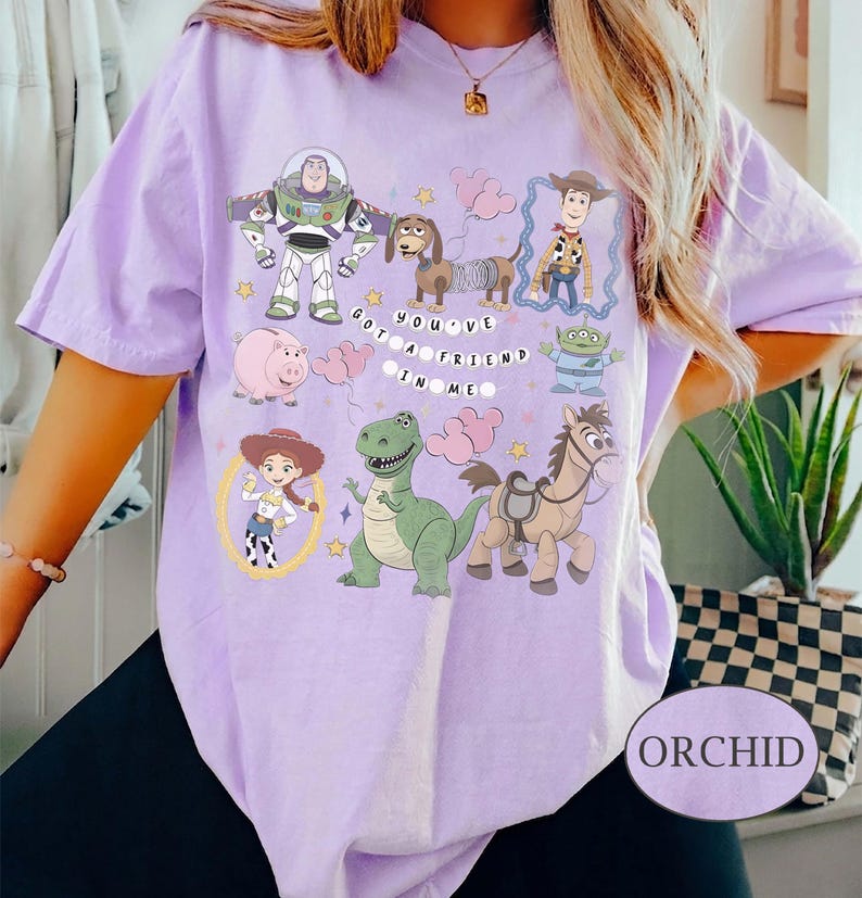 Pu&ograve; includere: T-shirt color orchidea con una grafica di personaggi di un popolare film d'animazione. Il design include Buzz Lightyear, Woody e altri personaggi, con la frase "You've Got a Friend in Me."