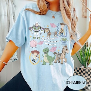 Pu&ograve; includere: T-shirt azzurra con personaggi dei cartoni animati di Toy Story. Il design include Buzz Lightyear, Woody, Jessie e altri personaggi, con la scritta "GOT YOU'VE A FRIEND IN ME". La maglietta &egrave; realizzata in materiale morbido.