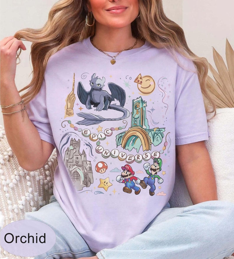 May include: Orchid-colored t-shirt with a colorful graphic design featuring a dragon, castle, Mario and Luigi, and the words "EPIC UNIVERSE". The shirt has a crew neck and short sleeves.