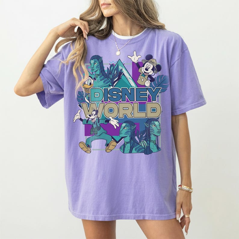 Puede incluir: Una camiseta de color morado claro con un estampado gr&aacute;fico que incluye el texto DISNEY WORLD. El dise&ntilde;o presenta ilustraciones de Mickey Mouse, Goofy, Donald y personajes de Avatar sobre un fondo geom&eacute;trico con hojas tropicales.