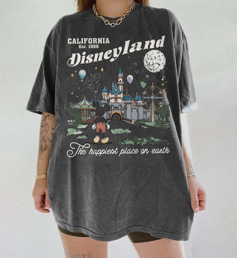 Puede incluir: Camiseta gris oscuro con un gr&aacute;fico de Disneyland. El gr&aacute;fico presenta un castillo, Mickey Mouse y el texto "California Est. 1955 Disneyland The happiest place on earth."