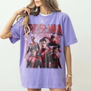 May include: A lilac t-shirt with a graphic of Spider-Man and the text "SPIDER-MAN Peter Parker" in red and white. The design features multiple images of Spider-Man in action poses, with lightning effects.