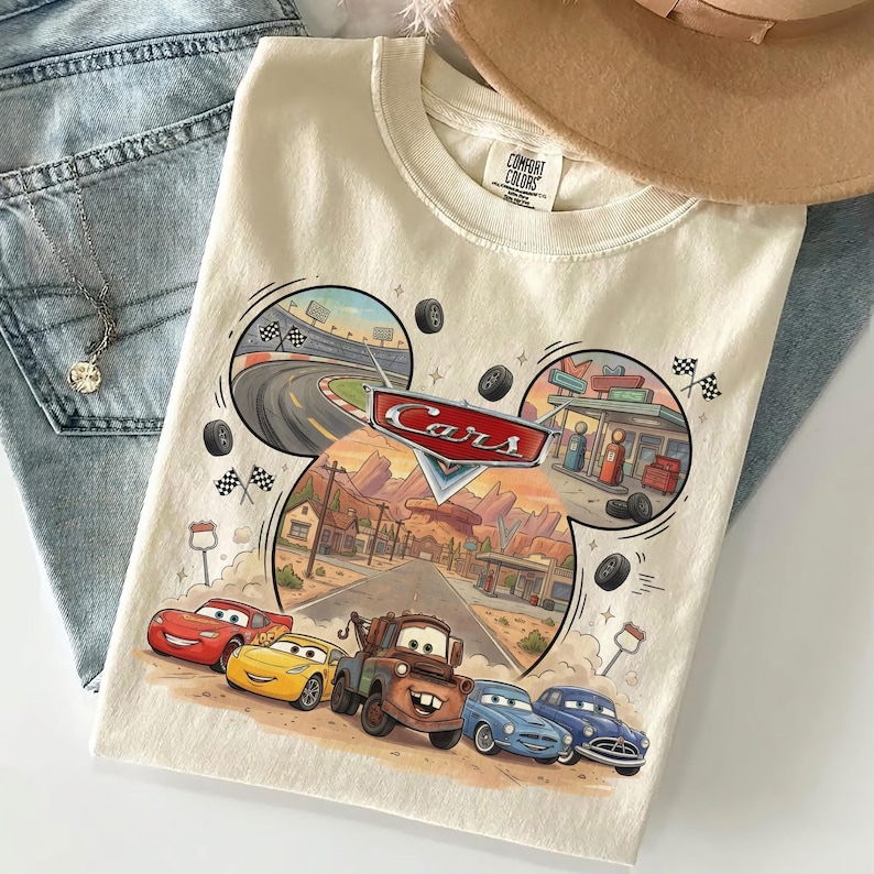Puede incluir: Una camiseta de color crema con un estampado gr&aacute;fico del logotipo de Disney Pixar Cars y personajes como Rayo McQueen, Mate y otros veh&iacute;culos. El dise&ntilde;o incluye un circuito de carreras, un pueblo del desierto y banderas a cuadros.